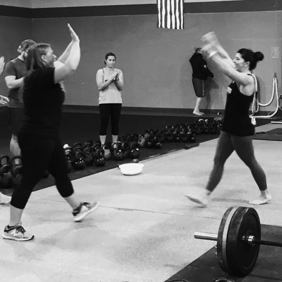 Two ladies about to share a high-five after one completed a heavy barbell deadlift at a Tactical Strength Challenge.